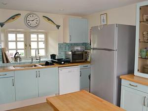 a kitchen with a refrigerator and a clock on the wall at Reids Cottage in Lairg