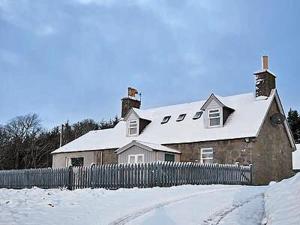 una casa con techo cubierto de nieve y valla en Reids Cottage, en Lairg