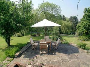 una mesa y sillas con una sombrilla en un patio en Wee Bridge Farm Cottage, en Mobberley