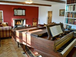 a living room with a piano and a fireplace at Dyes Cottage in Hindolveston