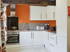 a kitchen with white cabinets and an orange wall at Granary Cottage in Penrhyn Bay
