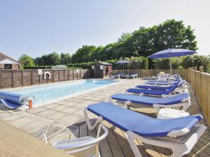 a row of blue chairs and umbrellas next to a swimming pool at Lintel Barn - E5253 in Runcton Holme