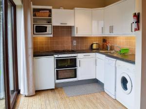cocina con armarios blancos, lavadora y secadora en Boundary Gallery Cottage, en Framlingham