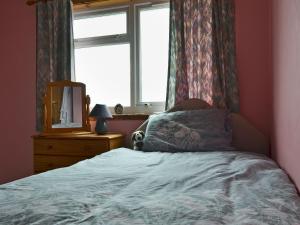 Schlafzimmer mit einem Bett, einem Fenster und einem Spiegel in der Unterkunft Bute Cottage in Daliburgh