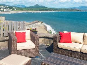 two wicker chairs with red pillows sitting on a balcony overlooking the ocean at Wendon in Criccieth