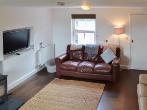 a living room with a brown leather couch and a flat screen tv at Rhos Y Grug in Llangwnadl