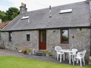 uma mesa e cadeiras em frente a um chalé de pedra em Ross Cottage em Cairneyhill