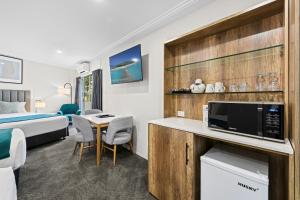 Habitación de hotel con cama y escritorio con TV. en Palm Court Motor Inn, en Port Macquarie