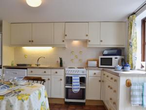 uma cozinha com armários brancos, um fogão e uma mesa em Pear Tree Cottage em Kinlet
