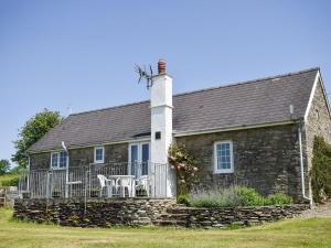 a stone house with a white chimney and two chairs at Cych Cottage in Capel-Ifan