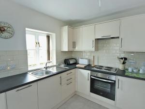 a kitchen with white cabinets and a sink and a window at Wisteria Cottage - E5094 in Chapel Saint Leonards