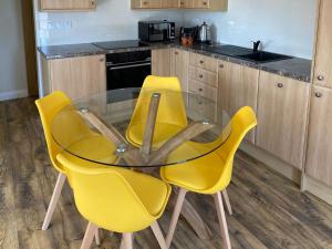 a kitchen with a glass table and two yellow chairs at Tregarthen Cottage in Perranuthnoe