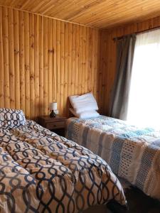 two beds in a room with wooden walls and a window at Cabaña El Sol Pehuenche Cordillera Talca SanClemente in Talca