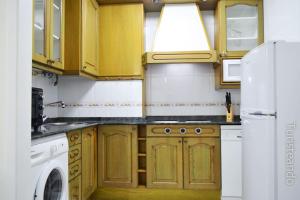 cocina con armarios de madera, lavadora y secadora en APARTAMENTO BARLOVENTO en San Vicente de la Barquera