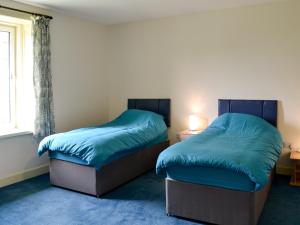 a bedroom with two beds with blue sheets and a window at Bonshawside Farmhouse in Kirtlebridge
