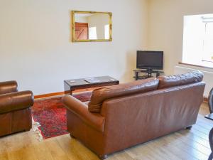 a living room with a leather couch and a television at Broomstick Cottage in Elsdon