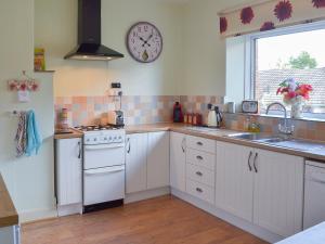 a kitchen with white cabinets and a clock on the wall at Lavender Cottage in Buckfastleigh