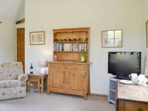 a living room with a television and a book shelf at Stable Cottage in Ticehurst