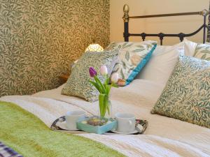 a tray with a vase of flowers and two cups on a bed at Larkspur in Hollington