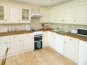 a white kitchen with white cabinets and wooden floors at Peartree Cottage in St Mellion