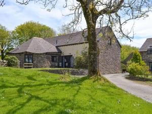 a stone house with a tree in the grass at Willow Cottage in Woolfardisworthy