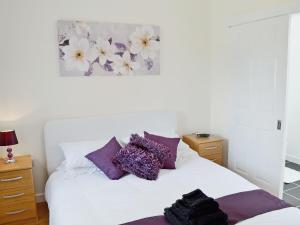 a bedroom with a white bed with purple pillows at Myrtle Cottage - 28177 in Fairgirth