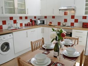 uma cozinha com uma mesa com cadeiras e um lavatório e uma mesa com flores em Myrtle Cottage - 28177 em Fairgirth
