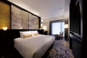 金沢市にあるTHE HOTEL SANRAKU KANAZAWAの大きなベッドとデスクが備わるホテルルームです。