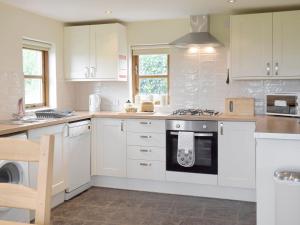 a kitchen with white cabinets and a stove top oven at Bryncrwn Cottage in Rhyd-y-felin