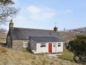 una pequeña casa con una puerta roja en una colina en Glentairre Cottage - Swww, en Balnaboth