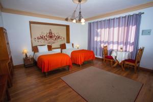 1 dormitorio con 2 camas con sábanas de color naranja y mesa en Centenario Inn, en Cusco