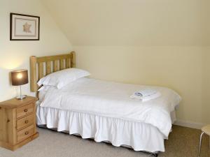 a bedroom with a bed with white sheets and a lamp at Birch Cottage in Glenrossal