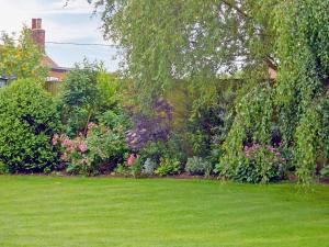 a garden with a green lawn with flowers and trees at Wold View Cottage in Rillington