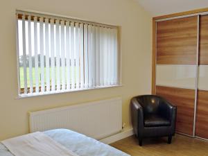 a bedroom with a black chair and a window at Oak Cottage in Winthorpe