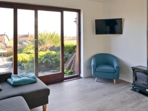 a living room with a blue chair and a television at Eider Cottage in Embleton