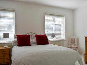 a bedroom with a bed with red pillows and two windows at Shingle Cottage in Whitstable