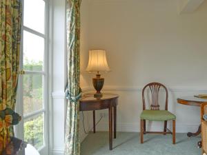 a table with a lamp and a chair next to a window at Acorn Cottage in Todenham