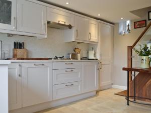 a white kitchen with white cabinets and a tile floor at Weavers Cottage in Stow on the Wold