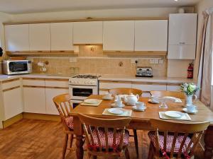 una cocina con mesa de madera con sillas y una cocina con armarios blancos. en Mill Cottage, en Winterborne Steepleton