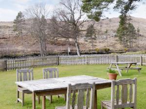 a wooden table and chairs in a yard with a fence at Rowan Cottage in Glenrossal