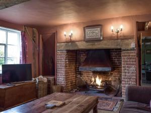 a living room with a brick fireplace and a tv at Bell Corner Cottage in Cratfield