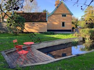 two red chairs and a table on a wooden deck next to a pond at Bell Corner Cottage in Cratfield