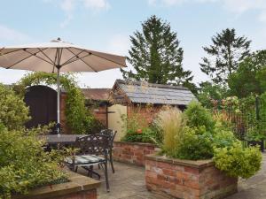 a patio with a table and an umbrella in a garden at Hurdlemakers Loft in Upper Brailes
