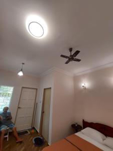 a man sitting in a chair in a bedroom with a ceiling fan at Margereth Cottage in Kuala Penyu