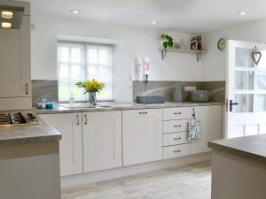 a white kitchen with white cabinets and a sink at Barton Cottage in North Petherwin