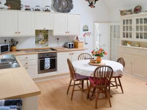 Boreland of ColvendにあるHolly Cottage - 28140のキッチン(白いキャビネット、テーブル、椅子付)