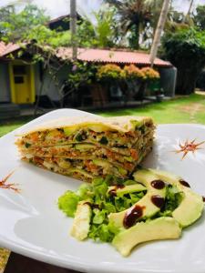 un sándwich y ensalada en un plato blanco en Plantation Surf Inn & Restaurant, en Midigama East