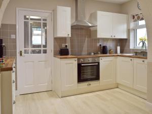 a kitchen with white cabinets and an open door at Glebe Cottage in Mautby