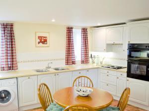 uma cozinha com armários brancos e uma mesa com cadeiras em The Linhay em East Worlington