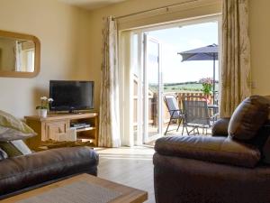 sala de estar con sofá, TV y balcón en Bramble Cottage en Shotton